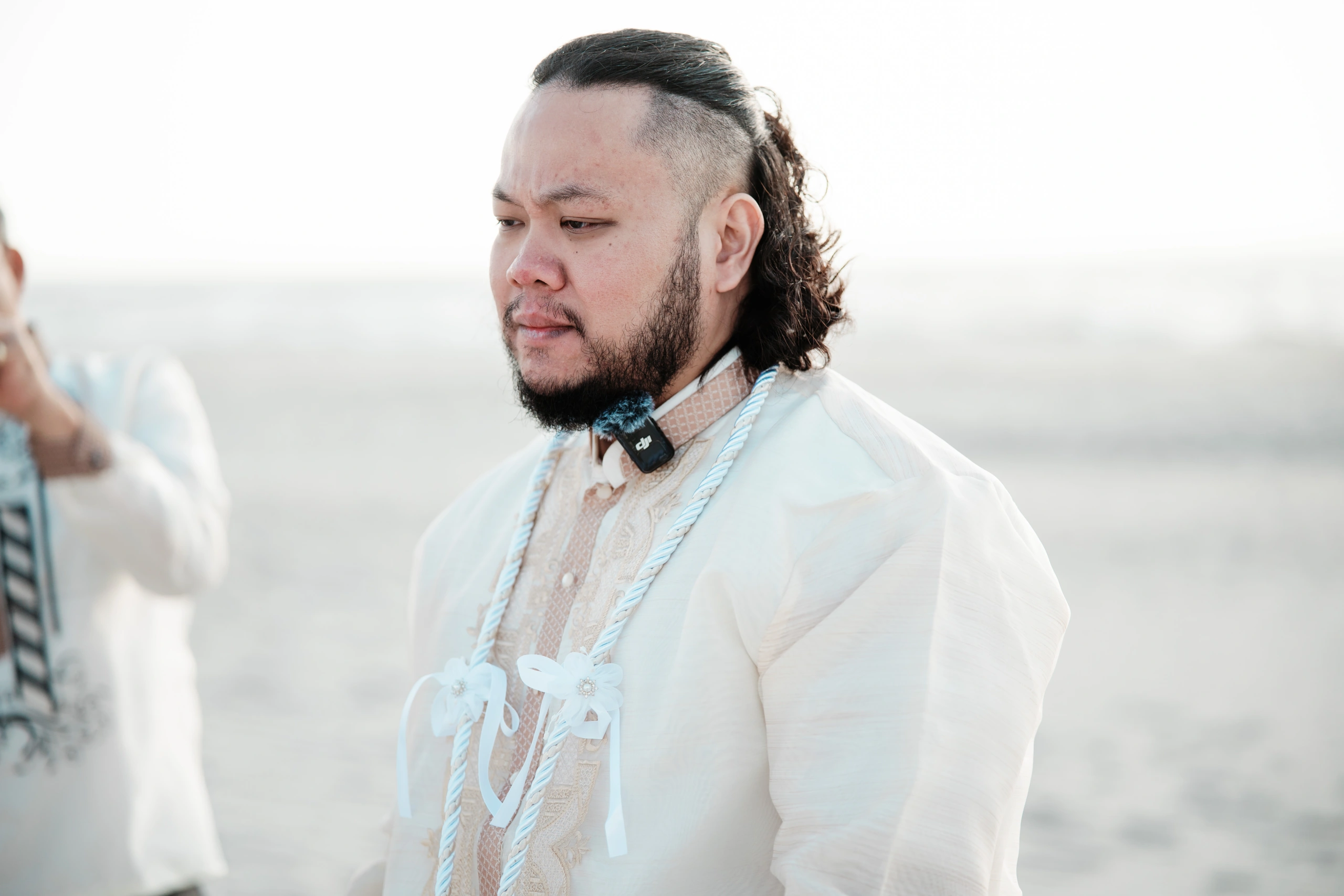 Person in a white winter jacket and loose jeans sits casually on bleachers at an outdoor field.