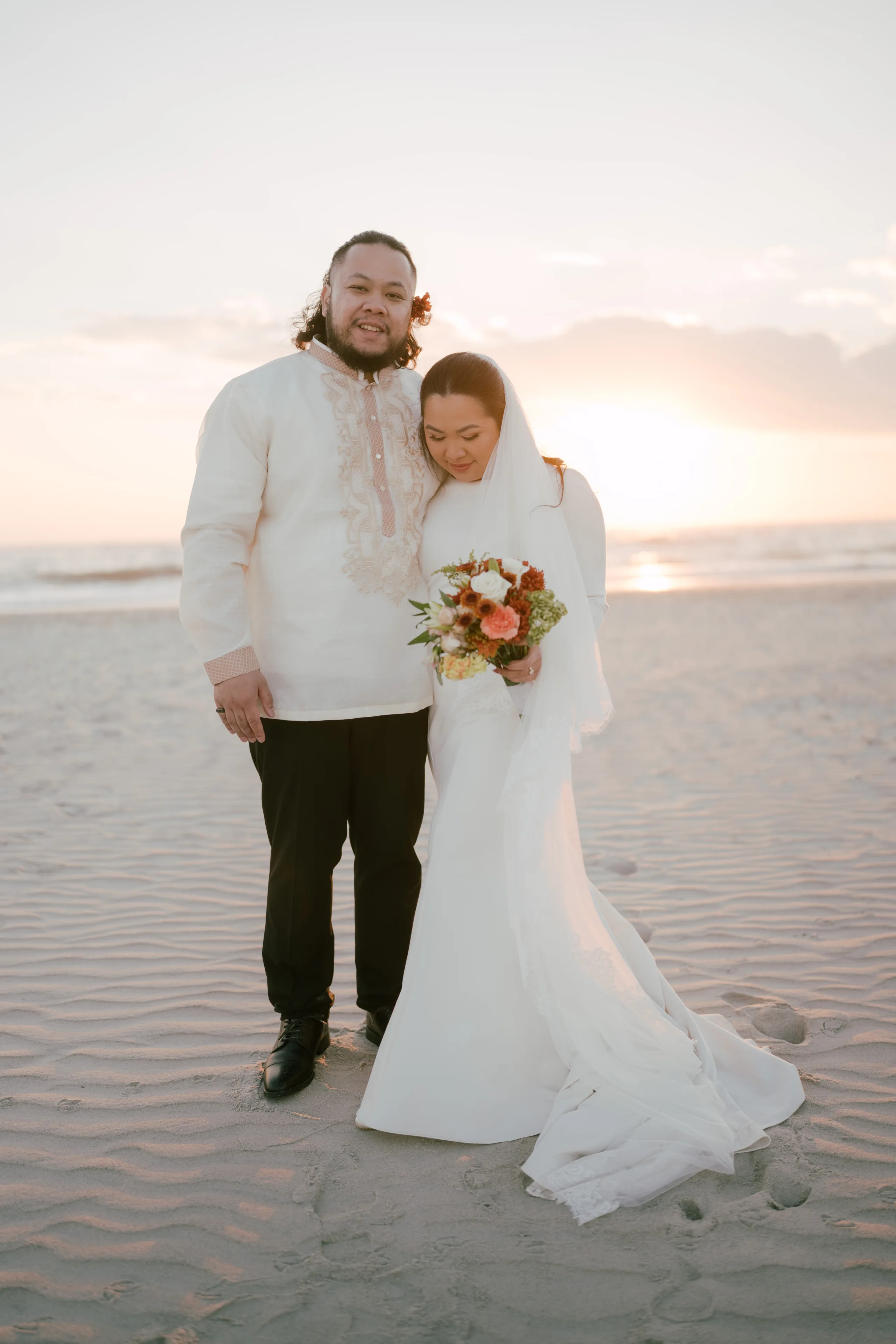 Formal couple in evening attire at outdoor event with autumn foliage background.